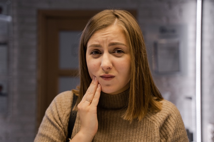 girl in light brown sweater with hand up to her mouth indicating tooth sensitivity