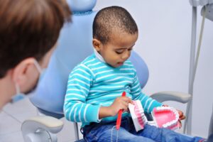 child playing with model teeth in dentist chair