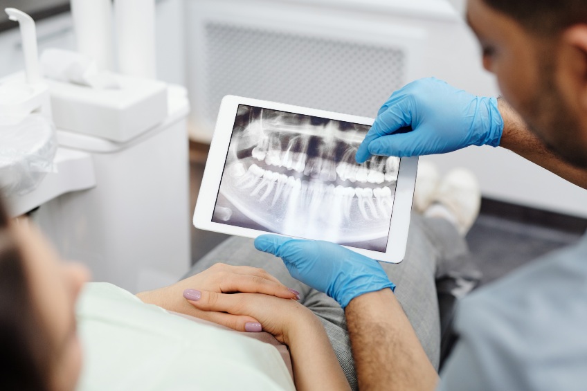 Dentist with blue gloves reviewing dental x-ray with patient.