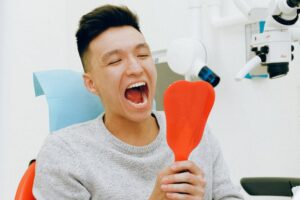 Man opening mouth looking into mirror at dentist office.