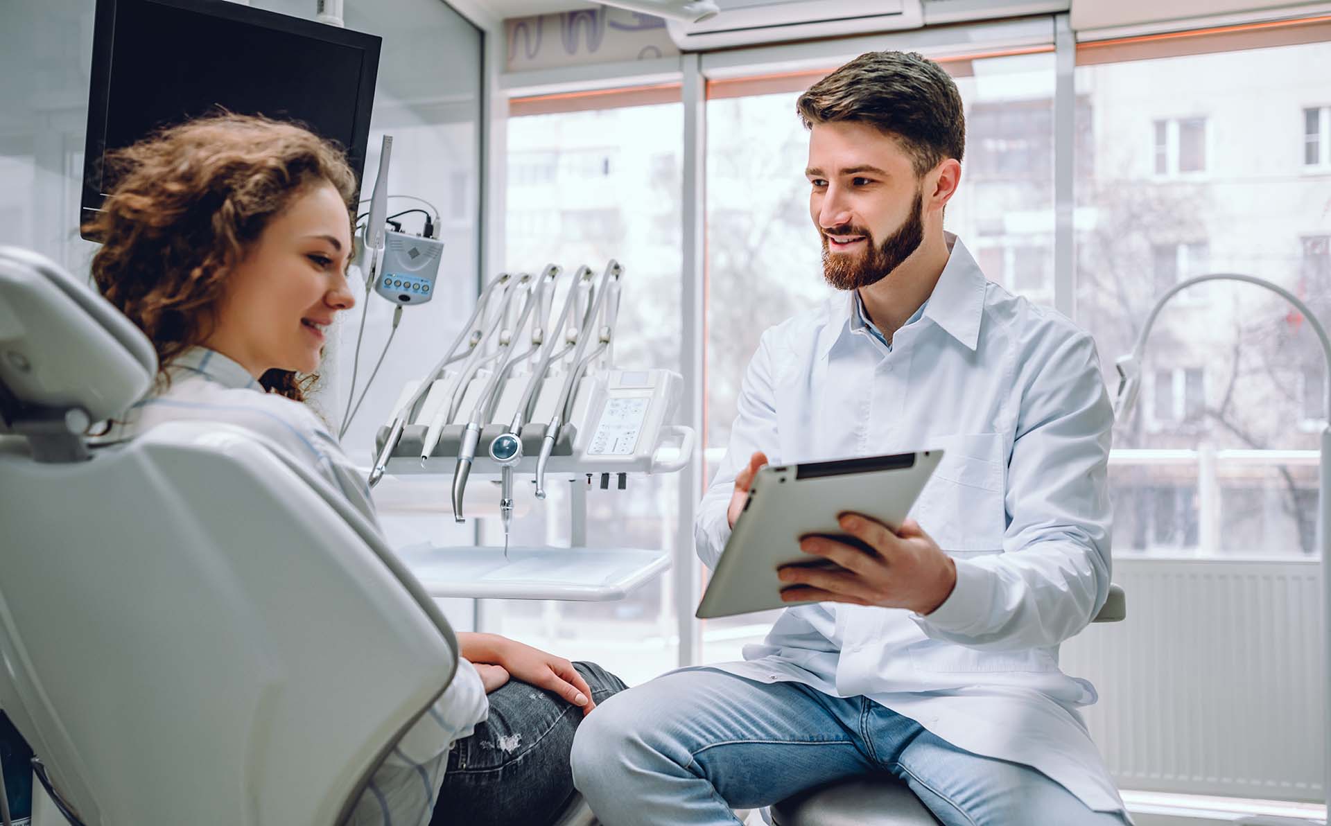happy male dentist showing tablet computer to woman patient at dental clinic office.