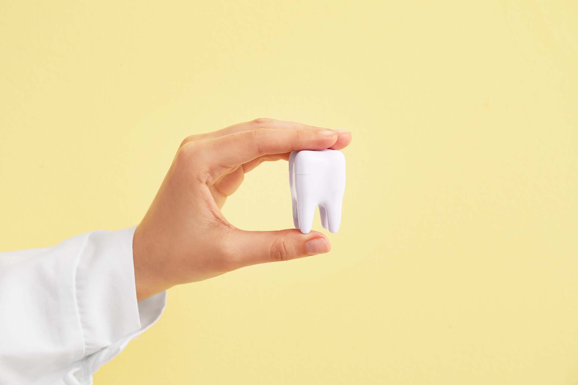 Hand of dentist with tooth on color background