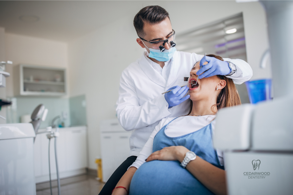 A pregnant woman sits in a dentist's exam chair during a dental procedure.